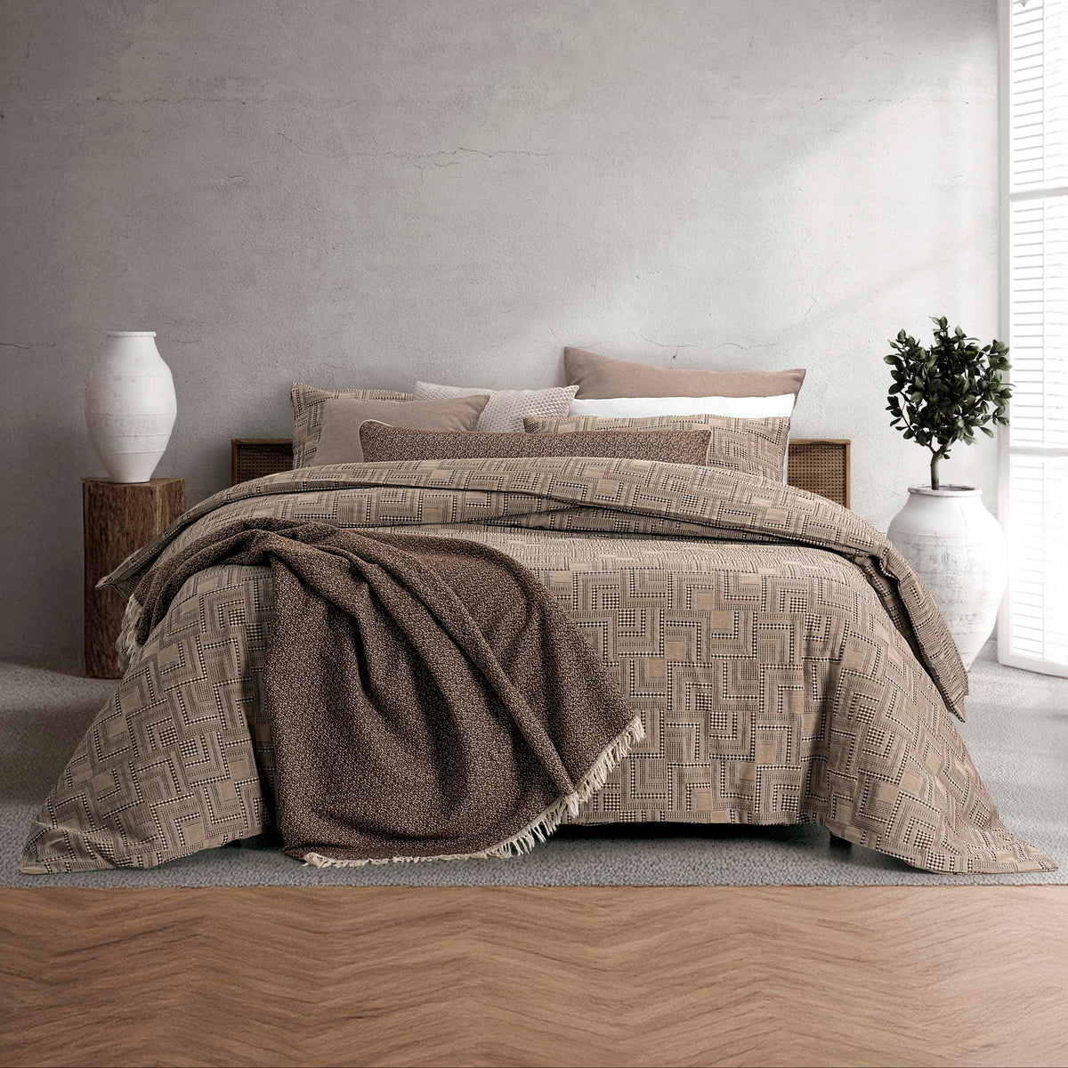 Capa de Edredão Fugi Castanho em 100% algodão jacquard, com padrão geométrico, apresentada numa cama de casal com manta decorativa