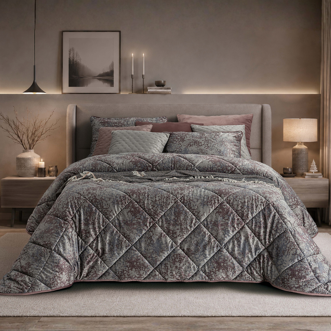 Edredão Conforter Novel em veludo digital, com padrão floral em tons cinza e rosa, apresentado numa cama de casal em um plano mais envolvente