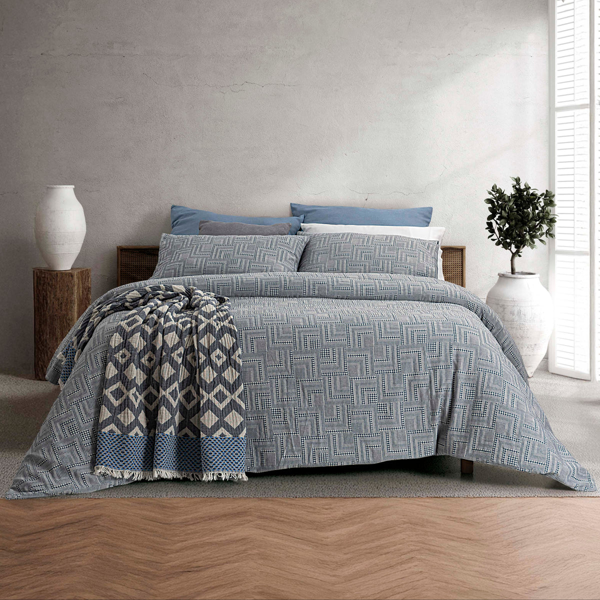 Capa de Edredão Fugi Azul em 100% algodão jacquard, com padrão geométrico, apresentada numa cama de casal com manta decorativa
