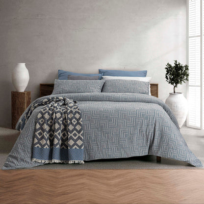 Capa de Edredão Fugi Azul em 100% algodão jacquard, com padrão geométrico, apresentada numa cama de casal com manta decorativa